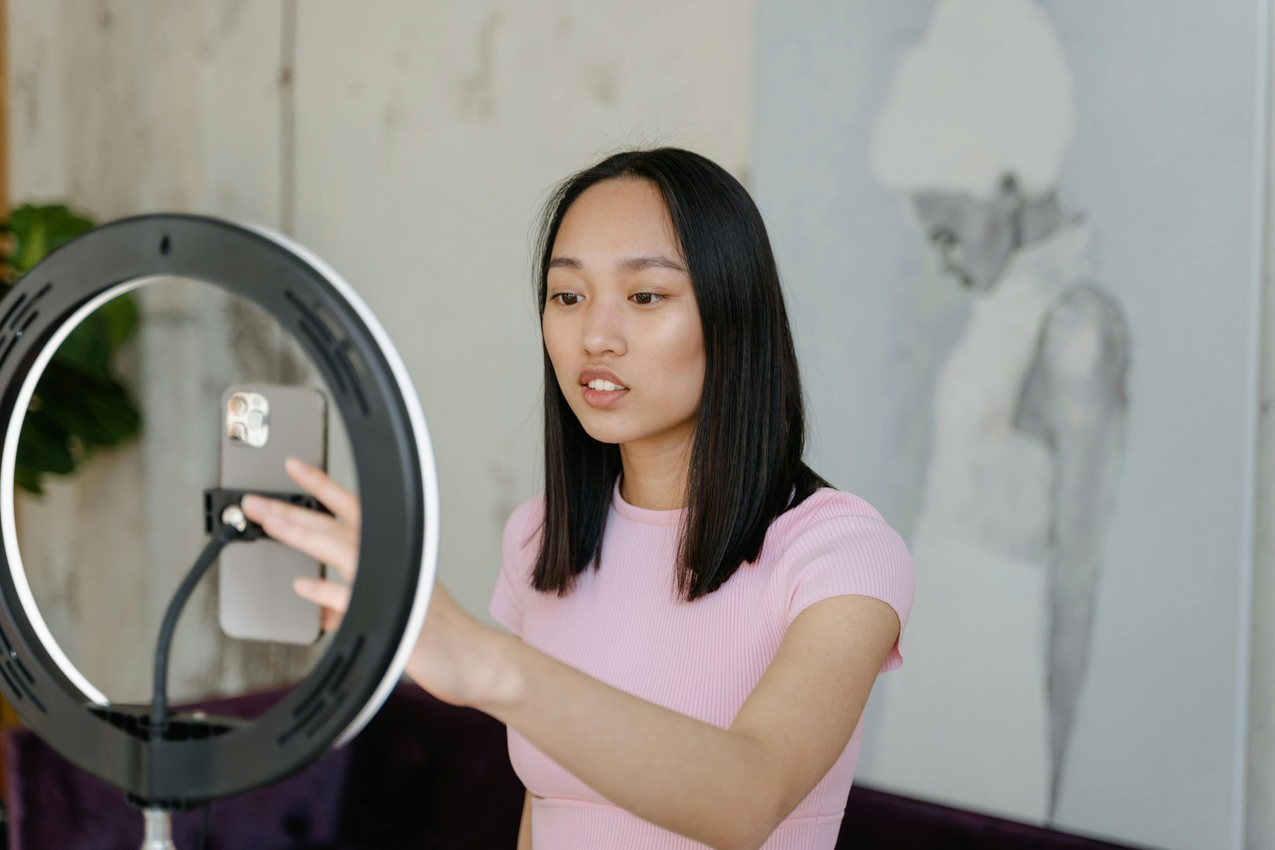 Young woman using a smartphone and ring light for social media content indoors.